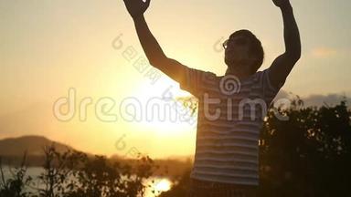 年轻人戴着太阳镜，在美丽的夕阳下举起双臂，慢吞吞地<strong>站在山顶</strong>上。1920x1080个
